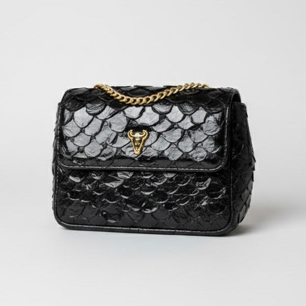 Black textured handbag with gold chain strap on a light gray background. pirarucu bags
